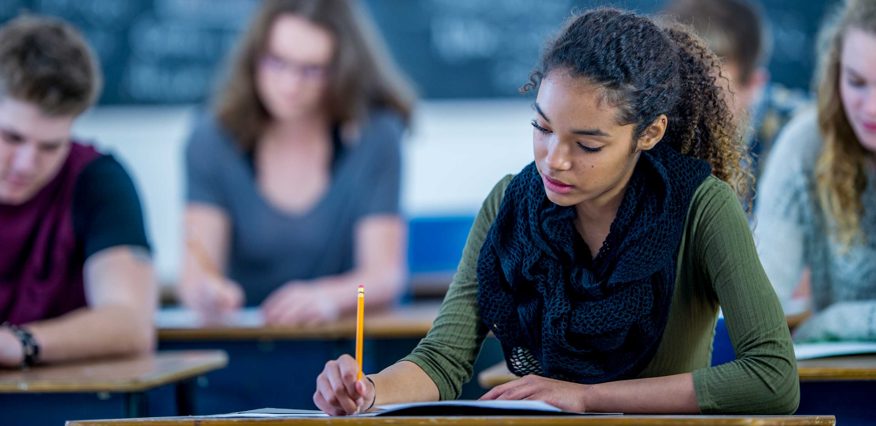 Student writing at her desk in a classroom